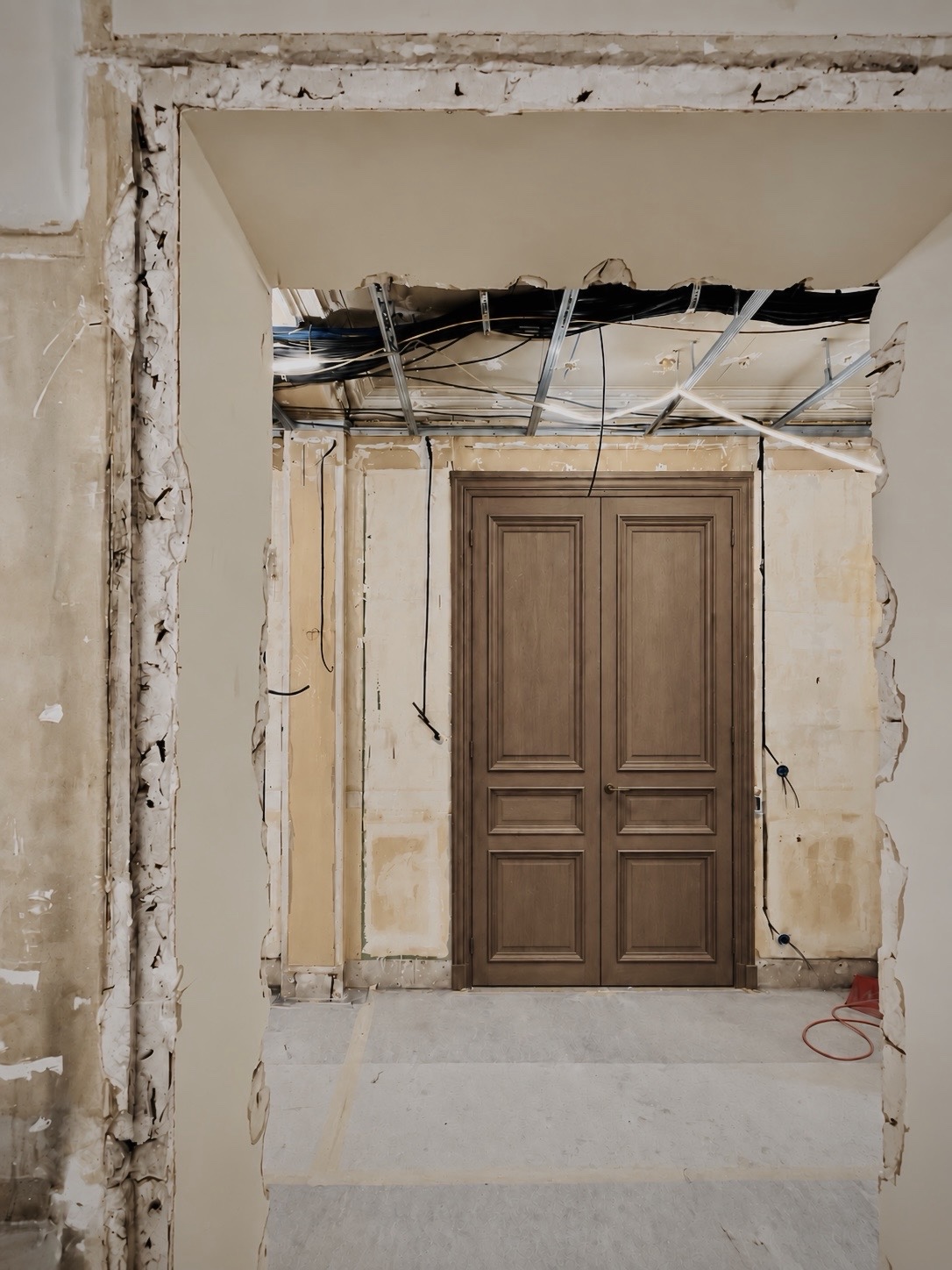Porte en bois ancienne ouverte sur un chantier de rénovation : murs en démolition, fils apparents et travaux en cours