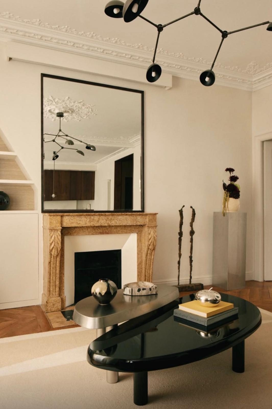 Salon haussmannien rénové : cheminée en pierre, grand miroir, tables basses sculpturales et moulures préservées