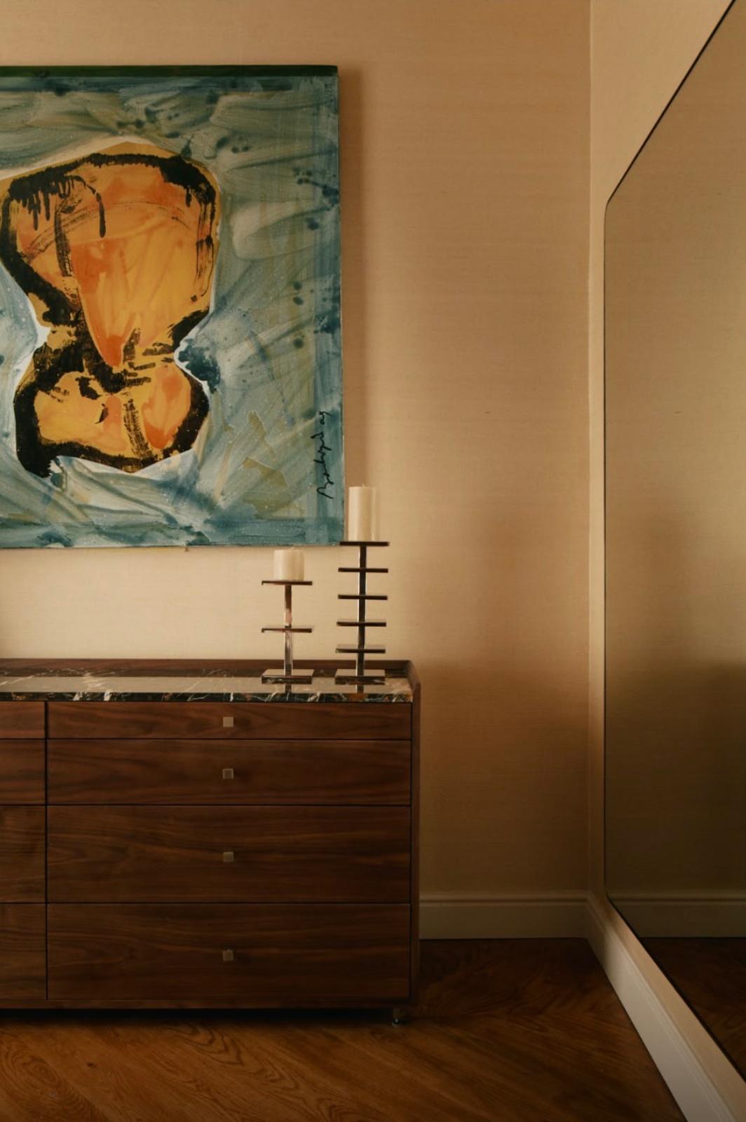 Commode en bois, tableau abstrait et bougeoirs dans une pièce restaurée